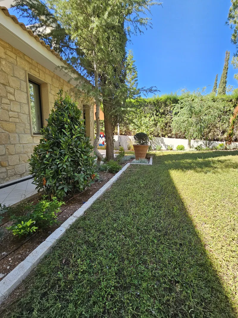 A lawn along the stone-clad house, edged with a bed of shrubs