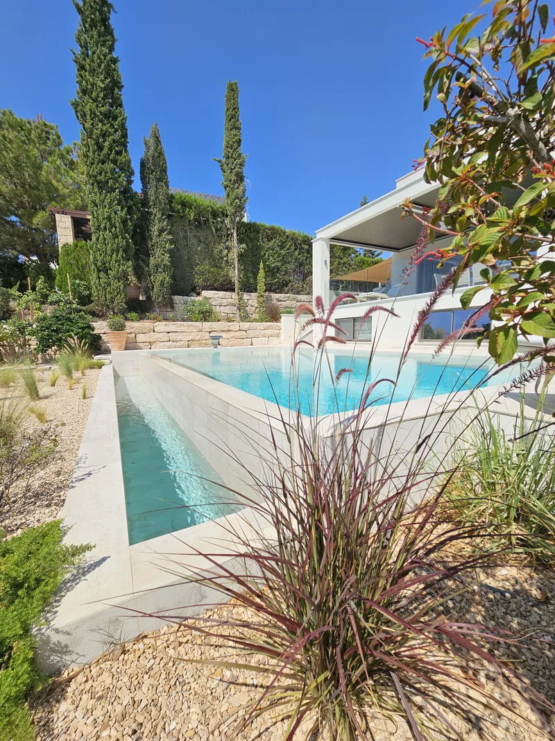 Red fountain grass beside the pool and its narrow water channel, cypresses beyond