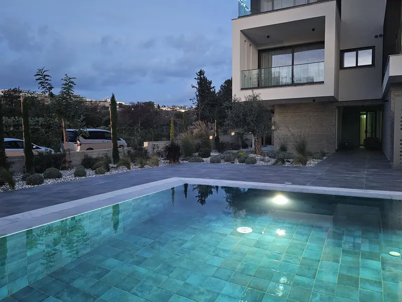 The pool lit at dusk, with gravel beds of shrubs and young trees around it