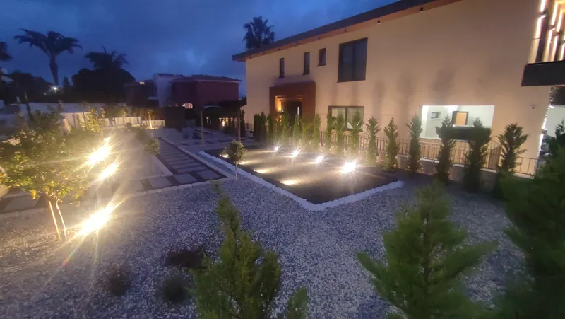 The gravel garden lit at dusk, with the pétanque court and a row of cypresses along the house
