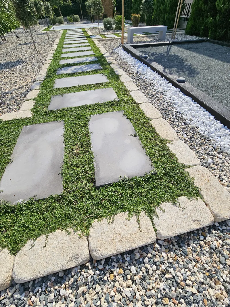 Square stepping stones in green ground cover, edged with stone, beside the pétanque court