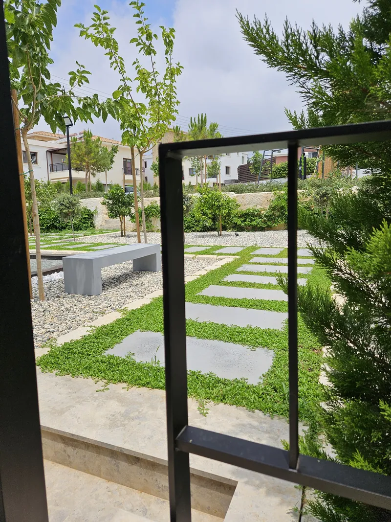 Square stepping stones in green strips, benches and young trees in a gravel garden