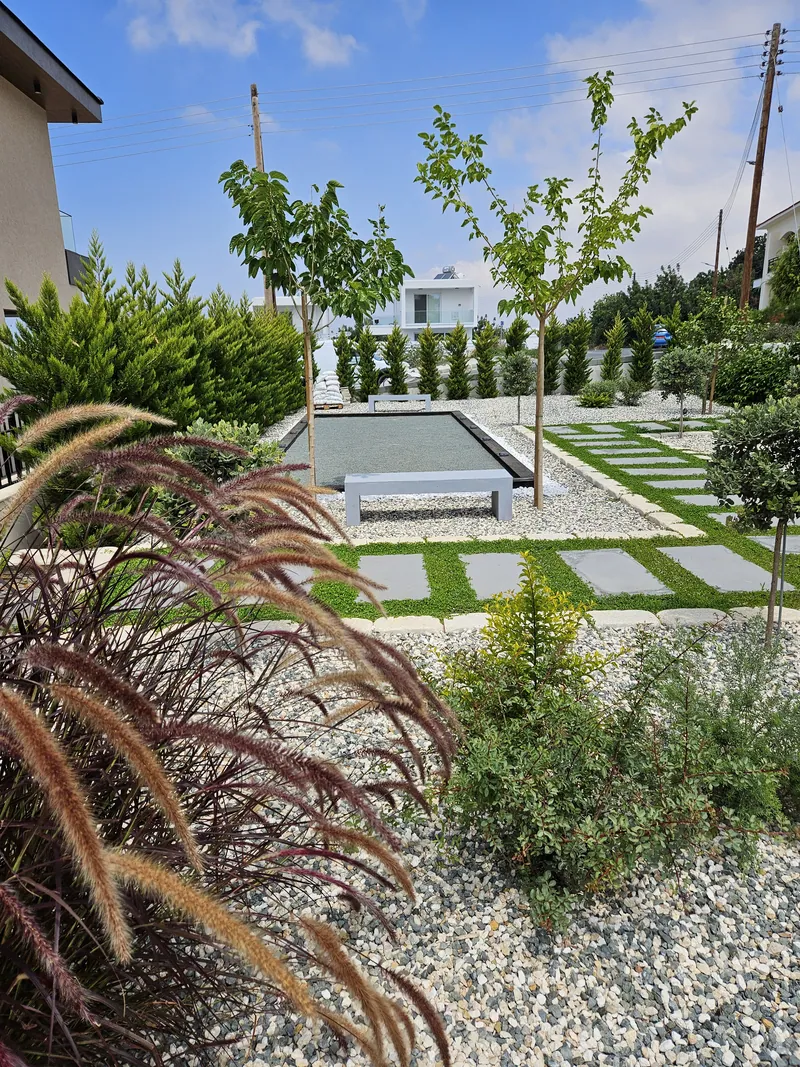 Red fountain grass and shrubs in gravel beside a reflecting pool and square stepping stones