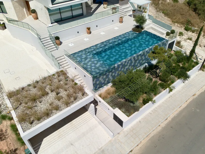 The pool terrace with terracotta pots, above a planted bed of olive trees and shrubs
