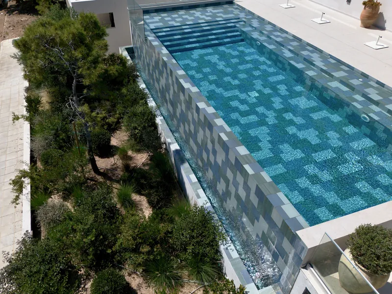 The tiled wall of the pool rising above olive trees and shrubs