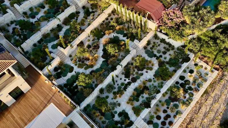 Curving beds of shrubs and grasses in white gravel between terrace walls, beside a timber deck