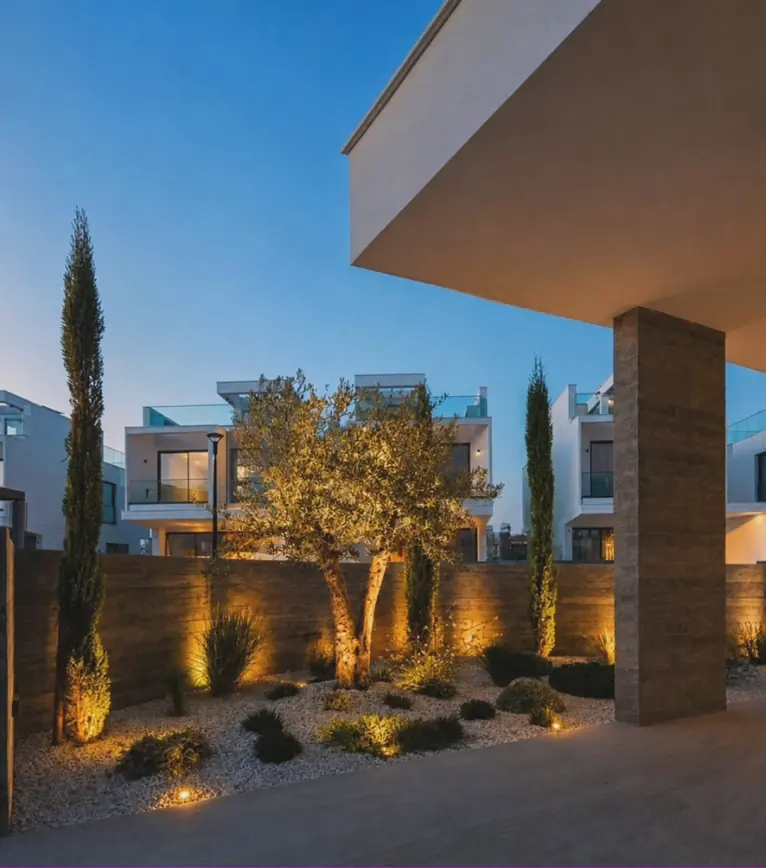 Garden lighting in Paphos: an olive tree and cypresses lit at dusk in a gravel garden beside modern villas